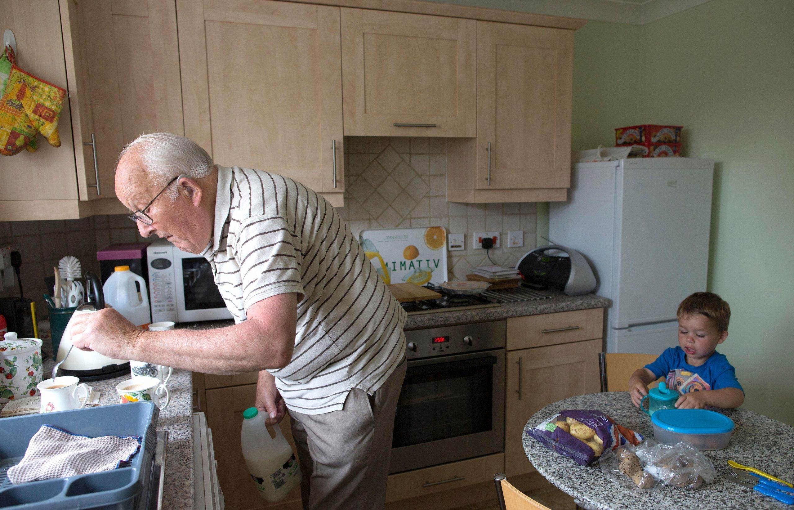 pensioner in kitchen making tea with little boy